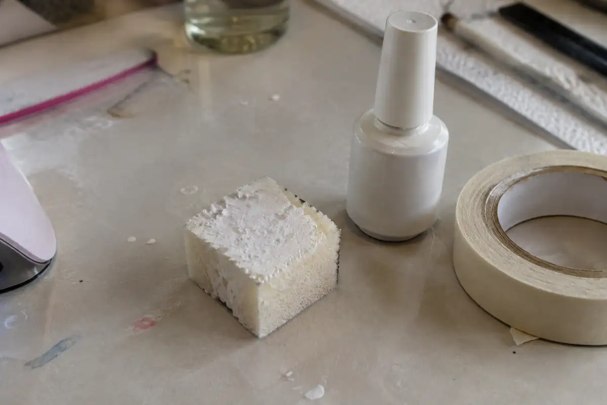 Éponge chargée de blanc à côté d'un flacon de gel et d'un rouleau adhésif sur une table de manucure