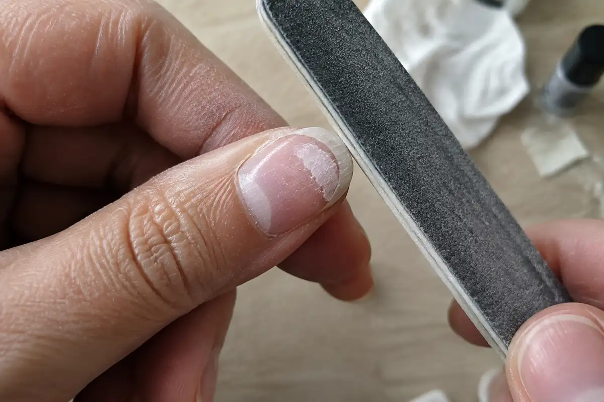 Gros plan d'un ongle dont le gel est à moitié limé, la lime à gros grain posée contre son bord