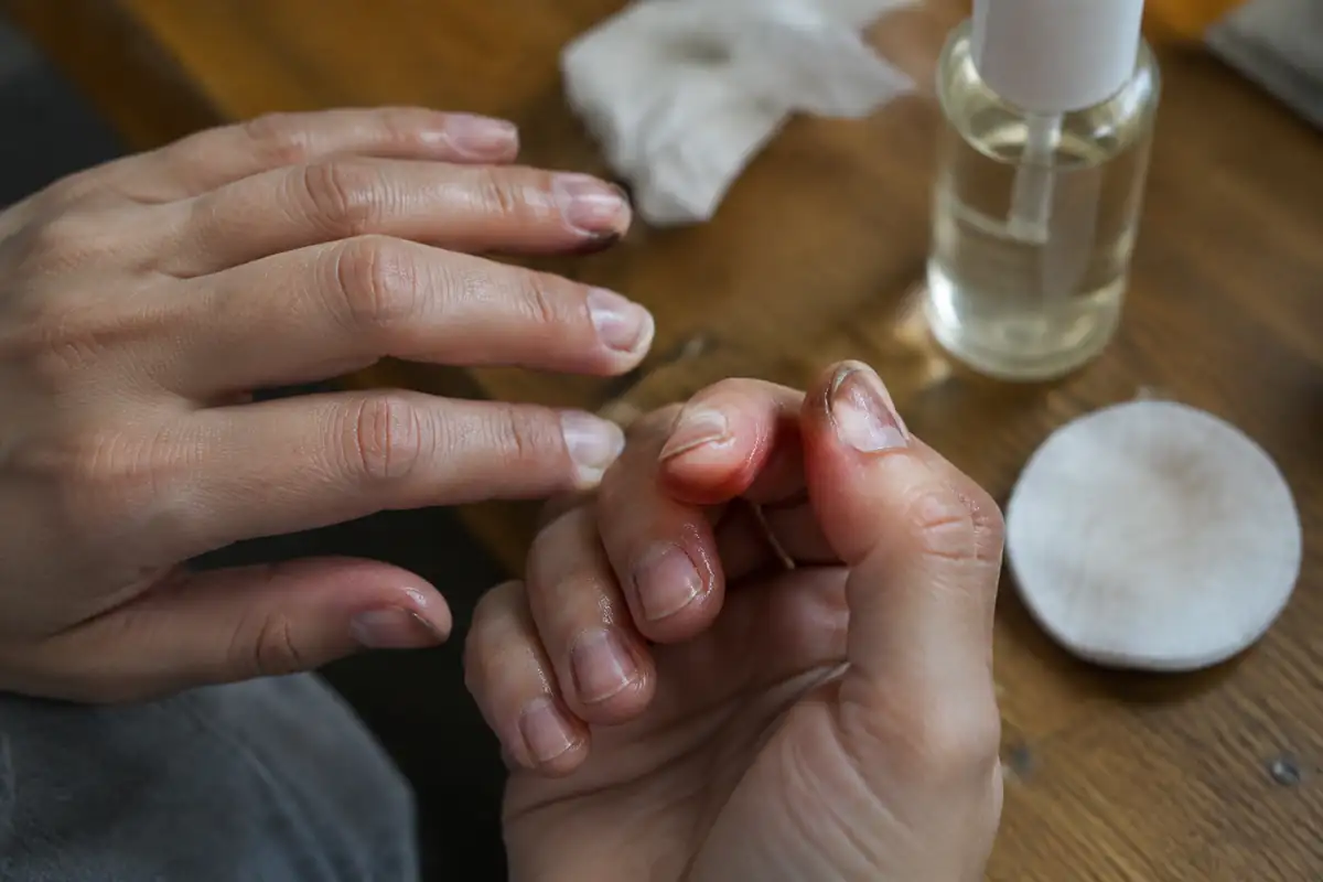Ongles nus après dépose du vernis, cuticules huilées, avec un coton et un petit flacon à l'arrière-plan